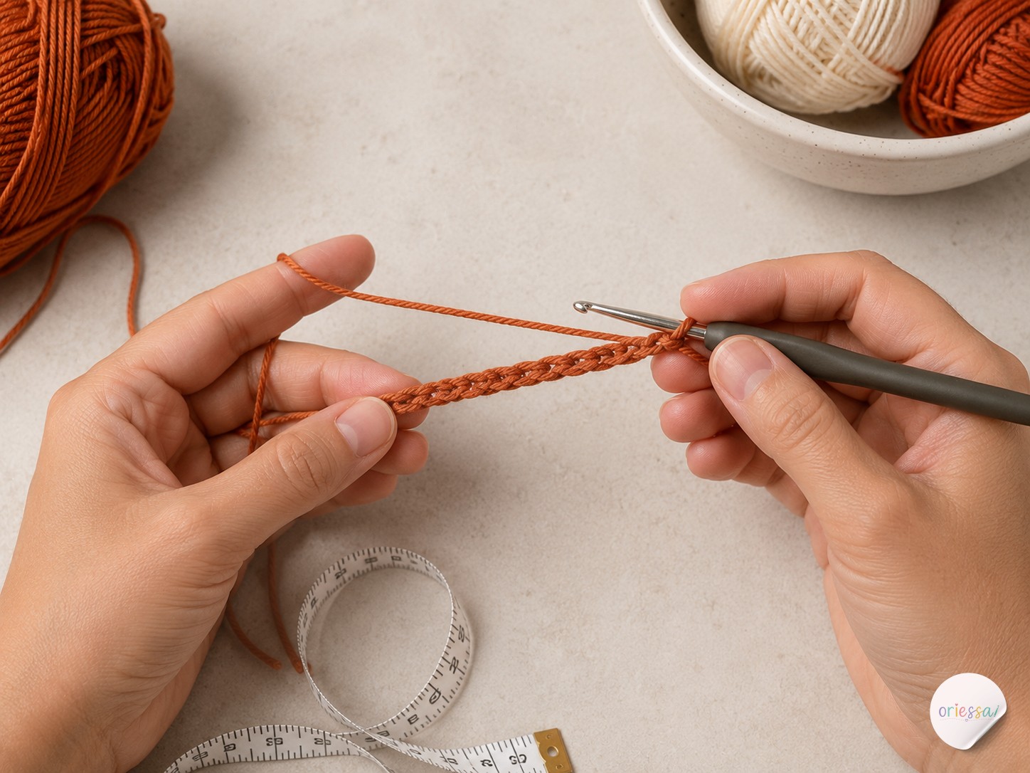 Hands crocheting a foundation chain with terracotta yarn