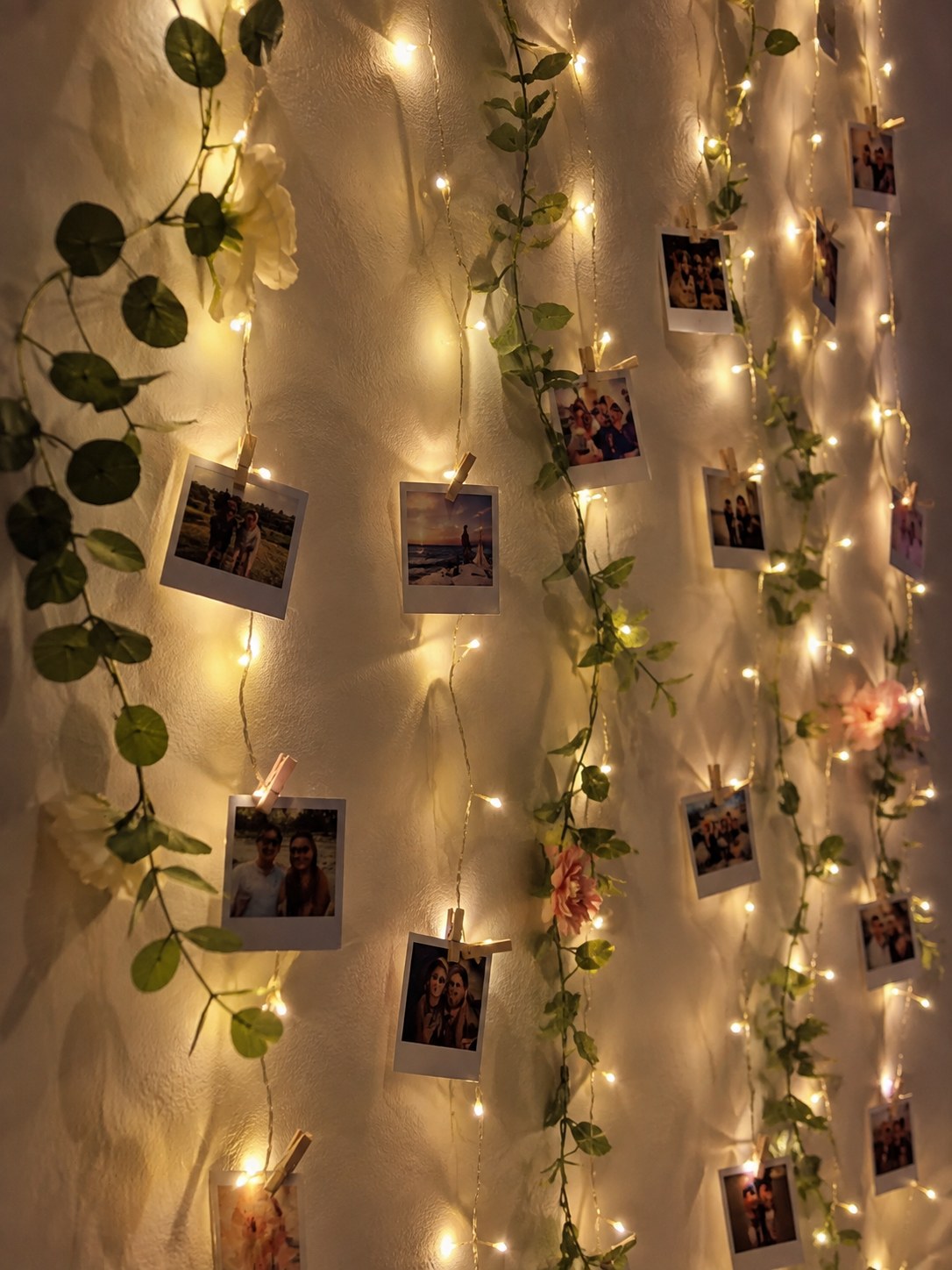 Fairy light photo wall woven with faux floral garland and clipped polaroid photos