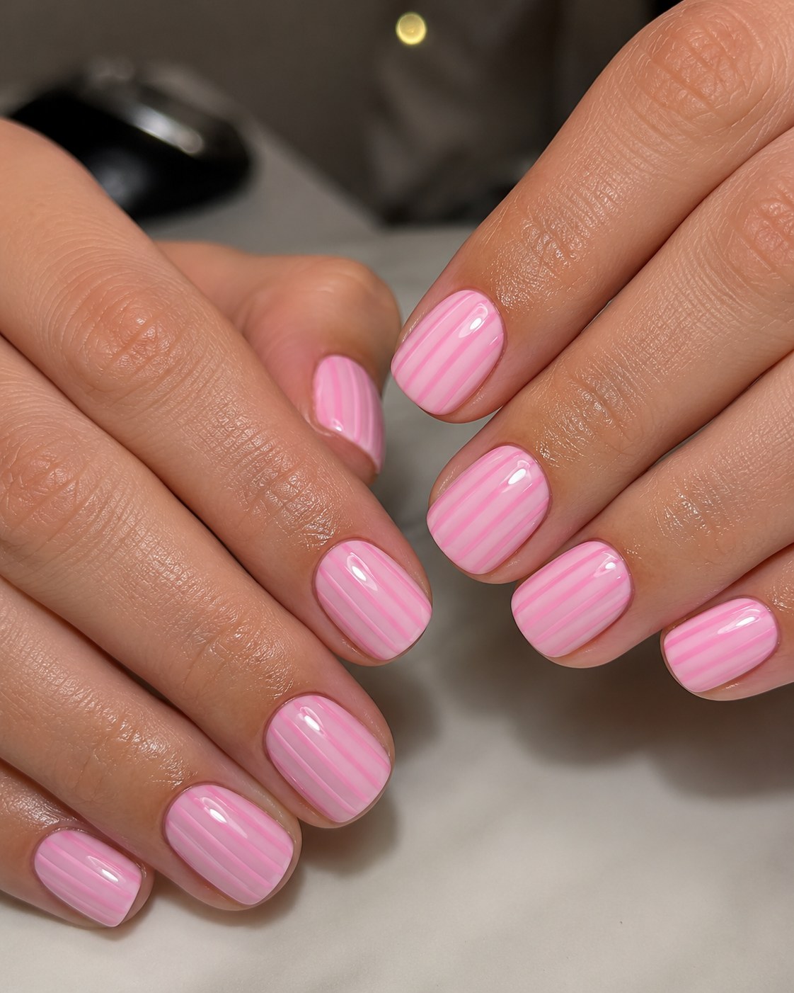 Pink short nails finished with fine white pinstripes for a candy-stripe manicure effect