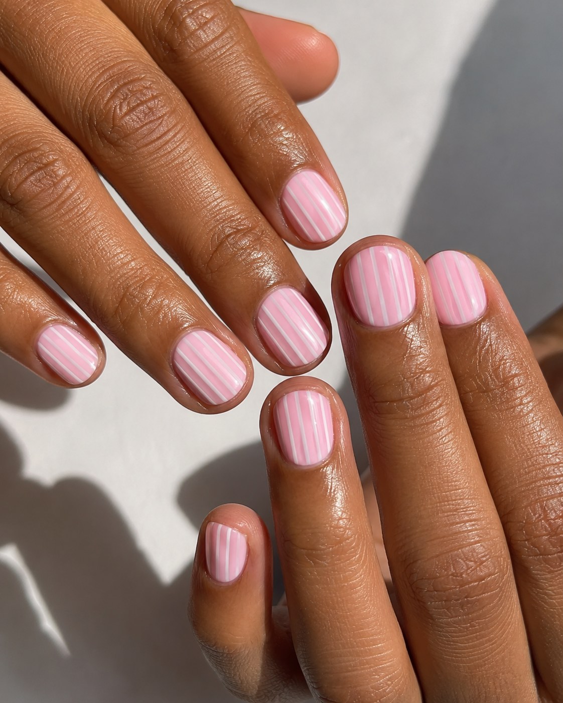 Pink short nails with white pinstripes shown on deeper skin tone with warm undertones