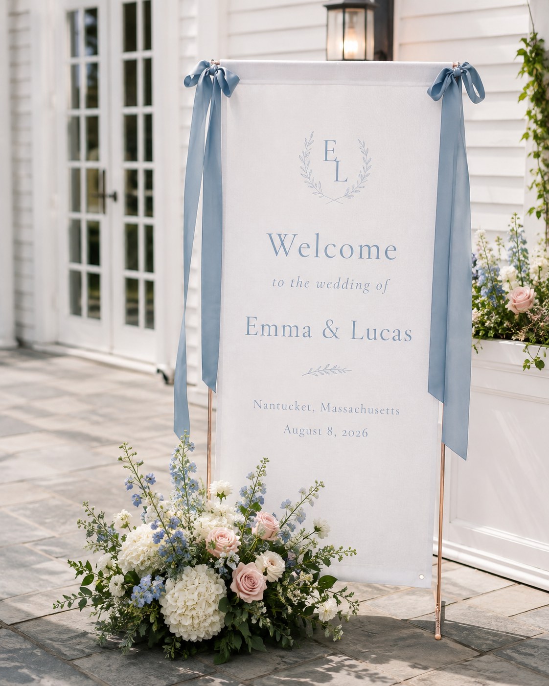 Fabric wedding welcome sign banner tied with dusty blue ribbon bows and a monogram crest